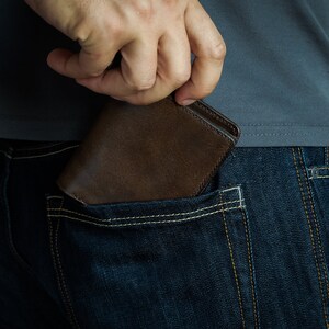 May include: A brown leather wallet being pulled out of a back pocket of blue jeans.