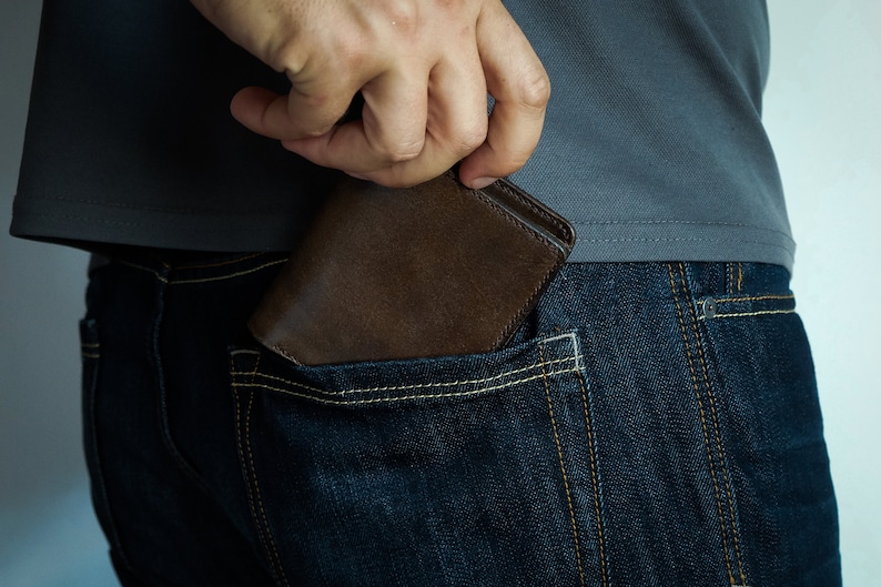May include: A brown leather wallet being pulled out of a back pocket of blue jeans.