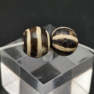May include: Two black and white striped agate beads. The beads are round and have a smooth, polished surface.