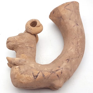 May include: A terracotta whistle shaped like a ram with a curved spout. The whistle has a detailed head with horns and a textured surface.
