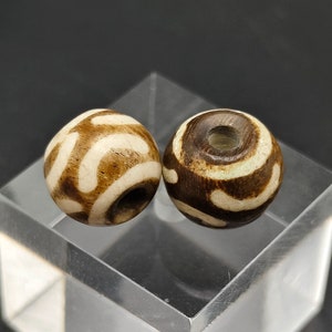 May include: Two brown and white agate beads with a hole in the center. The beads have a swirling pattern.