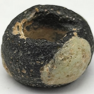 May include: A black and white glass bead with a hole in the center. The bead has a rough, textured surface.