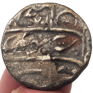 May include: A silver coin with Arabic script and a worn surface.