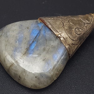 Peut inclure: Un pendentif en argent avec une grande pierre de labradorite gris clair irisée. L'argent est gravé d'un motif floral.