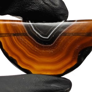 May include: A half-round agate cabochon with a brown and black banded pattern. The agate has a smooth, polished surface.