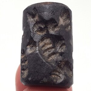 Könnte beinhalten: Ein schwarzer zylindrischer Stempel mit aufwendigen Schnitzereien. Der Stempel ist aus einem dunklen, glatten Material gefertigt und hat eine leicht strukturierte Oberfläche.