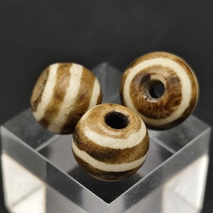 May include: Three brown and white striped beads with a hole in the center. The beads are made of a natural material and have a rustic look.