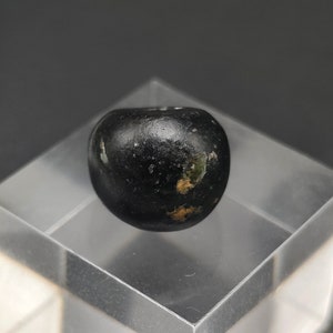 May include: A black, round bead with gold flecks. The bead is smooth and shiny.