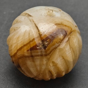 May include: A white and brown carved agate sphere with a swirling pattern. The sphere is smooth and polished.