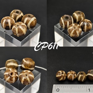 Op de afbeelding: Een set van zes ronde, bruin-wit gestreepte kralen. De kralen hebben een diameter van ongeveer 2,5 cm. De kralen zijn gerangschikt in twee groepen van drie. De kralen liggen op een wit oppervlak. CP611