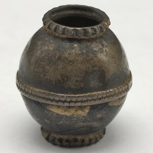 May include: A small, round, silver-colored metal container with a beaded rim and two bands of beads around the middle. The container has a slightly rounded bottom.