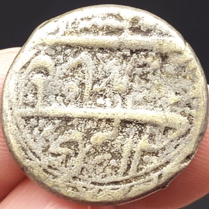 May include: A silver coin with Arabic script on both sides. The coin is worn and has a patina.