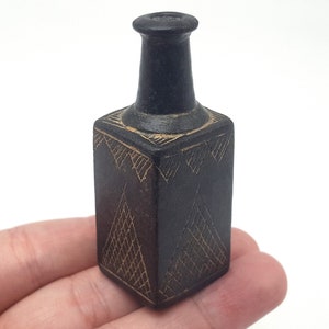 May include: A small, black ceramic bottle with a square body and a narrow neck. The bottle is decorated with intricate gold geometric patterns.