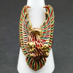 Op de afbeelding: Een gouden ring met een gedetailleerd ontwerp van een rode, groene en blauwe adelaar met uitgespreide vleugels.