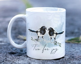 May include: White ceramic mug with a watercolor illustration of two magpies facing each other on a branch. The text "Two for joy" is written below the birds.