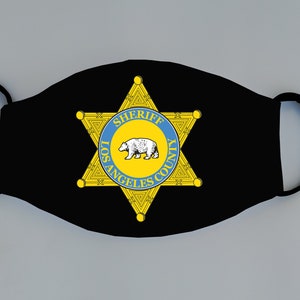 May include: Black face mask with a yellow star and a blue circle with the text "SHERIFF LOS ANGELES COUNTY" and a white bear inside the circle.