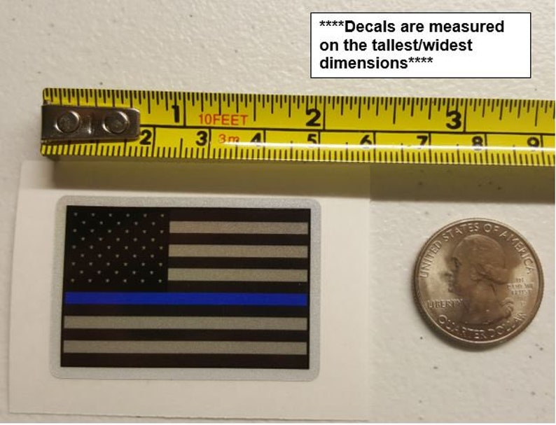 May include: A thin blue line American flag decal with a white background. The decal is measured on the tallest/widest dimensions. The decal is next to a ruler and a US quarter.