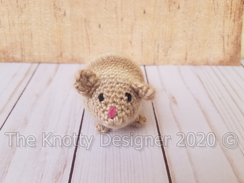 Peut inclure: Un animal en peluche crochet&eacute; ressemblant &agrave; un hamster, avec un sch&eacute;ma de couleurs brun clair et beige. L'animal a des yeux noirs et un nez rose.