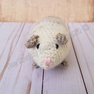 Peut inclure: Un animal en peluche crochet&eacute; ressemblant &agrave; un cochon d'Inde. L'animal est blanc avec des oreilles brunes et des yeux noirs. Il a un nez rose.