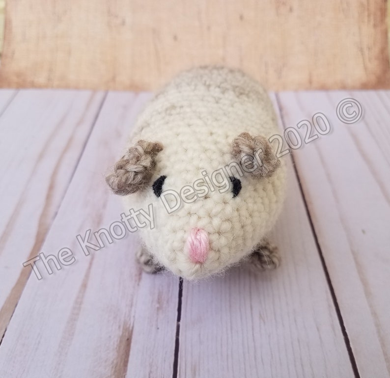 Peut inclure: Un animal en peluche crochet&eacute; ressemblant &agrave; un cochon d'Inde. L'animal est blanc avec des oreilles brunes et des yeux noirs. Il a un nez rose.