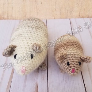 Peut inclure: Deux peluches de cobaye en crochet, l'une plus grande et l'autre plus petite. Le plus grand cobaye est blanc avec des accents bruns, tandis que le plus petit cobaye est brun avec des accents blancs. Les deux ont des yeux noirs et des nez roses.