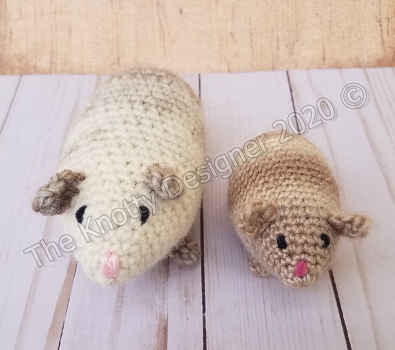 Peut inclure: Deux peluches de cobaye en crochet, l'une plus grande et l'autre plus petite. Le plus grand cobaye est blanc avec des accents bruns, tandis que le plus petit cobaye est brun avec des accents blancs. Les deux ont des yeux noirs et des nez roses.