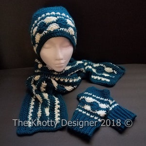 May include: Teal blue crocheted hat, scarf, and fingerless gloves with white accents. The hat has a white pompom on top. The scarf and gloves have a repeating pattern of white circles.