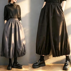 Puede incluir: Un top negro de manga larga con cuello alto combinado con una falda voluminosa hasta los tobillos, con cintura elástica y un dobladillo fruncido y plisado. El conjunto se completa con calcetines negros y mocasines negros de plataforma.