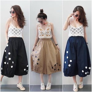Puede incluir: Tres conjuntos con un top de ganchillo blanco combinado con culottes. Los culottes son negros, beige y azul marino, cada uno adornado con grandes lunares blancos o negros. Los conjuntos se completan con zapatillas blancas.
