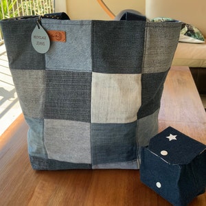 Peut inclure: Un sac cabas en jean bleu avec un motif patchwork. Le sac a une étiquette en cuir marron qui dit "Recyclage Jeans".