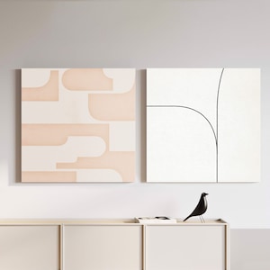 May include: Two square wall art pieces. One features a geometric pattern in cream and peach. The other has a black line drawing on a white background. A black bird sculpture sits on a cream-colored cabinet.