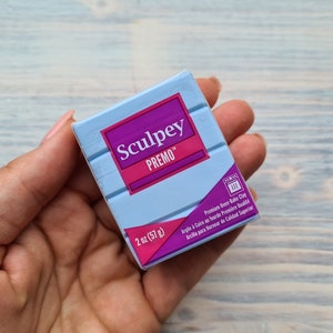 以下が含まれることがあります： Sculpey Premoオーブンベイククレイの青とピンクのパッケージ。パッケージには、ブランド名、製品名、重量（2オンス（57グラム））が記載されています。