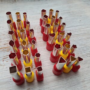 Può includere: Un set di 30 tagliapasta in metallo con manici rossi e gialli. I tagliapasta sono disposti in due file e presentano una varietà di forme, tra cui stelle, cuori, fiori e forme geometriche.