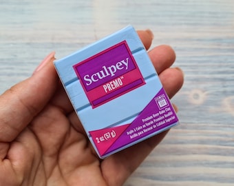 Pode incluir: Uma embalagem azul e rosa de argila para assar no forno Sculpey Premo. A embalagem é etiquetada com o nome da marca, o nome do produto e o peso: 2 oz (57 g).
