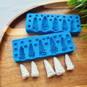 May include: Two blue silicone moulds with cone-shaped cavities and several white, cone-shaped objects. The moulds are rectangular with six cone impressions each. The cones are white with a textured surface. The items are on a wooden tray.