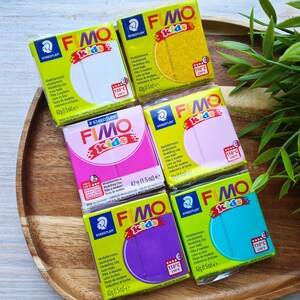 May include: Six different colors of FIMO Kids modeling clay, each in a 42g (1.5 oz) package. The colors are white, yellow, pink, purple, turquoise, and blue. The packages are all labeled with the FIMO Kids logo and the Staedtler brand name.