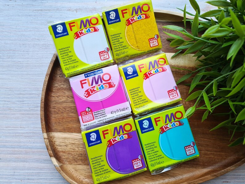May include: Six different colors of FIMO Kids modeling clay, each in a 42g (1.5 oz) package. The colors are white, yellow, pink, purple, turquoise, and blue. The packages are all labeled with the FIMO Kids logo and the Staedtler brand name.