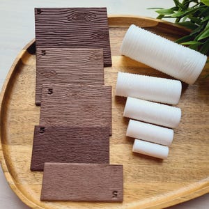 May include: A wooden tray holds several brown rectangular pieces with wood grain texture and the number "5" on them. Also, there are several white cylindrical pieces with a textured surface. Green foliage is in the background.