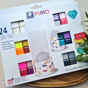 May include: A pack of 24 FIMO Effect polymer clay colours. The pack includes a range of colours, including red, blue, green, yellow, and purple. The pack also features a small candle holder made with FIMO clay. The pack is labelled with the FIMO logo and the text "Effect".