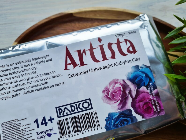 May include: A package of white air-drying clay, labeled "Artista Extremely Lightweight Airdrying Clay" with a 170 gram weight. The package features a 14+ age recommendation and a barcode. The clay is made by PADICO and is suitable for crafting projects.