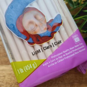 May include: A package of light-colored oven-bake clay. The package is labeled with the text "1 lb (454 g)", "Light | Claro | Clair", and "Professional Quality Oven-Bake Clay".