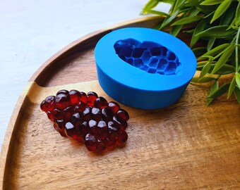 Puede incluir: Un molde de silicona azul con forma de panal de abejas, y un grupo de caramelos de gelatina rojos, translúcidos, sobre una superficie de madera.
