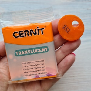 May include: A package of translucent polymer clay by Cernit. The package is orange and white with the brand name and product name printed on the front. The package is labeled with the text "Pâte polymère translucide, Translucent polymer clay, Transluzente Polymermasse, Pasta Polimerica traslucida, Arcilla polimérica translúcida".