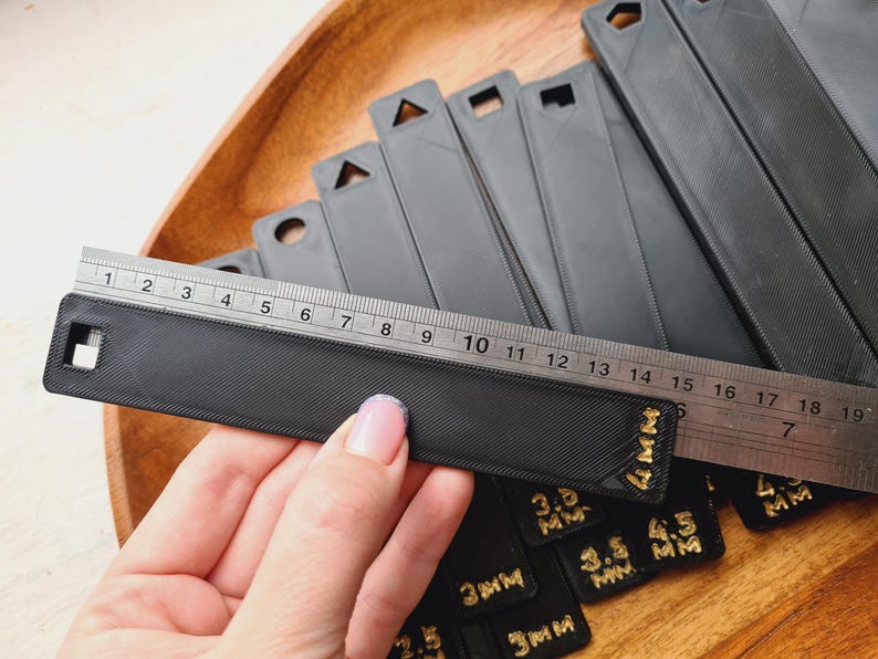 Peut inclure: Une r&egrave;gle noire avec une surface textur&eacute;e est plac&eacute;e sur un ensemble d'outils de mesure noirs. La r&egrave;gle est gradu&eacute;e en pouces et en centim&egrave;tres. Plusieurs outils de mesure noirs sont visibles, avec du texte dor&eacute; indiquant les mesures en millim&egrave;tres.