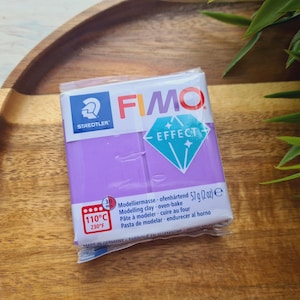 May include: A package of purple FIMO Effect modeling clay. The package has the brand name FIMO and the words "Effect" and "57g (2oz) e" printed on it. The package also includes instructions for baking the clay at 110°C or 230°F.