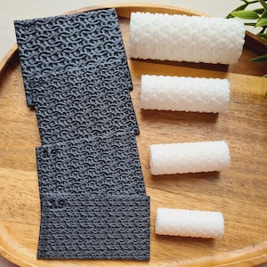 Peut inclure: Un plateau en bois présente un ensemble de dessous de verre texturés gris foncé et plusieurs objets cylindriques blancs. Les dessous de verre ont un motif en cotte de mailles. Les objets blancs ont une texture bosselée. Des feuilles vertes sont visibles.