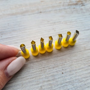 Peut inclure: Un ensemble de neuf outils en métal à manches jaunes avec des embouts de différentes formes. Les outils sont disposés en rangée sur une surface en bois clair.