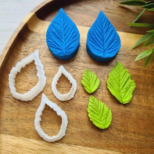 May include: A set of silicone moulds for baking and decorating cakes and other desserts. The moulds are shaped like leaves and are made of white silicone. There are also two blue silicone moulds shaped like leaves.