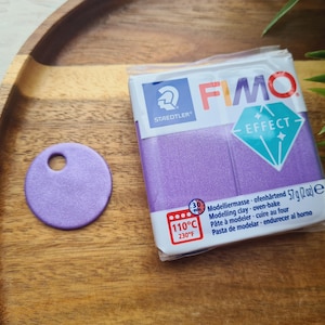 May include: A purple package of FIMO Effect modeling clay. The package has a white label with the FIMO logo and the text "Modelliermasse ofenhärtend 57g (2oz)". The package also has a temperature label that reads "110°C 230°F".