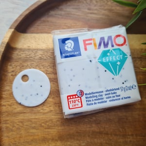 May include: A white package of FIMO Effect modeling clay with a blue and green diamond logo. The package has a red and white label with the text "110°C 230°F" and the text "Modelliermasse ofenhärtend 57g (202) e Modelling clay - oven-bake Pâte à modeler - cuire au four Pasta de modelar - endurecer al home".